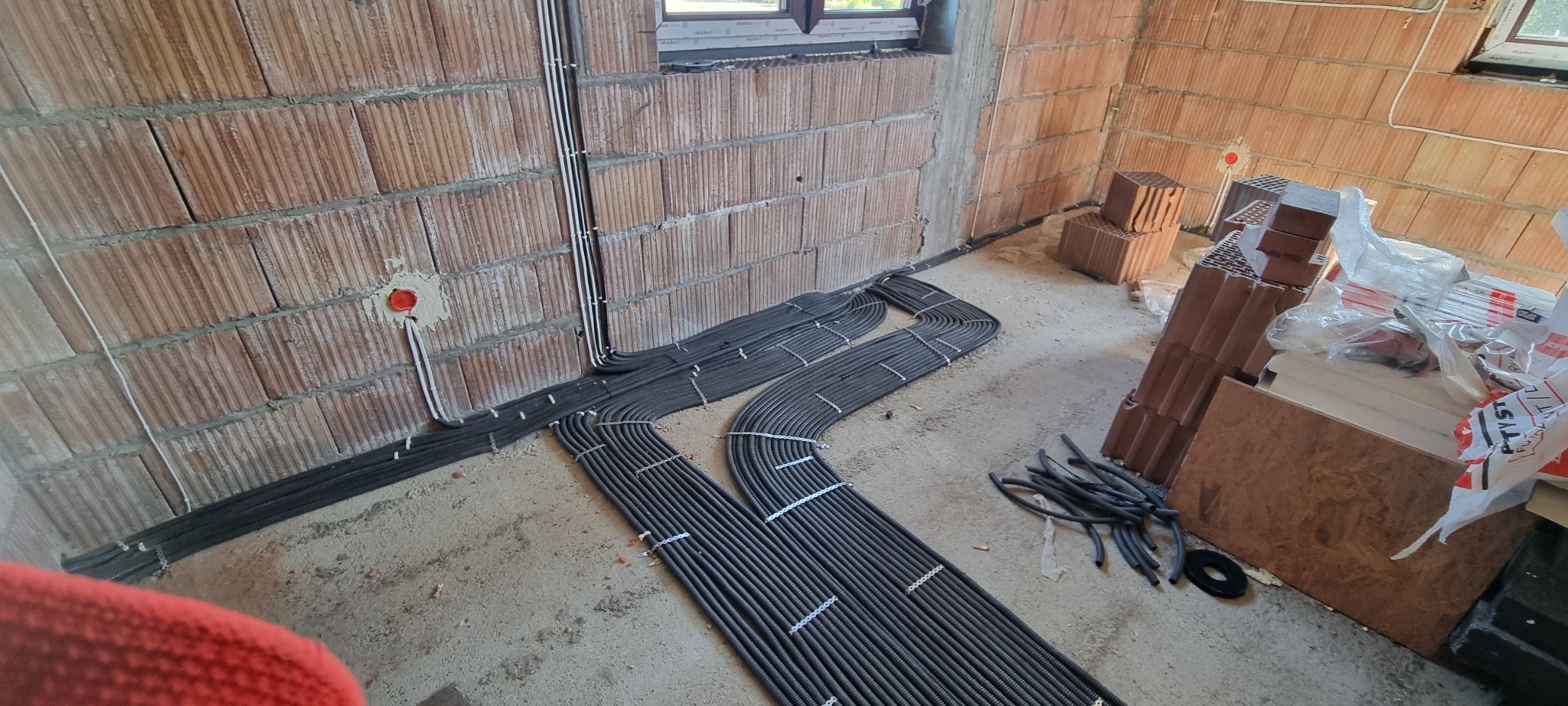 Instalacja elektryczna w surowym wnętrzu: kable w peszlach ułożone równolegle przy ścianach z cegły, widoczne puszki instalacyjne. Etap prac przed tynkowaniem.