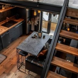 Holiarskyi Volodymyr - Loftowe wnętrze z drewnianą podłogą, czarną zabudową kuchenną i schodami z drewnianymi stopniami, widok z góry na stół z krzesłem i kanapą.