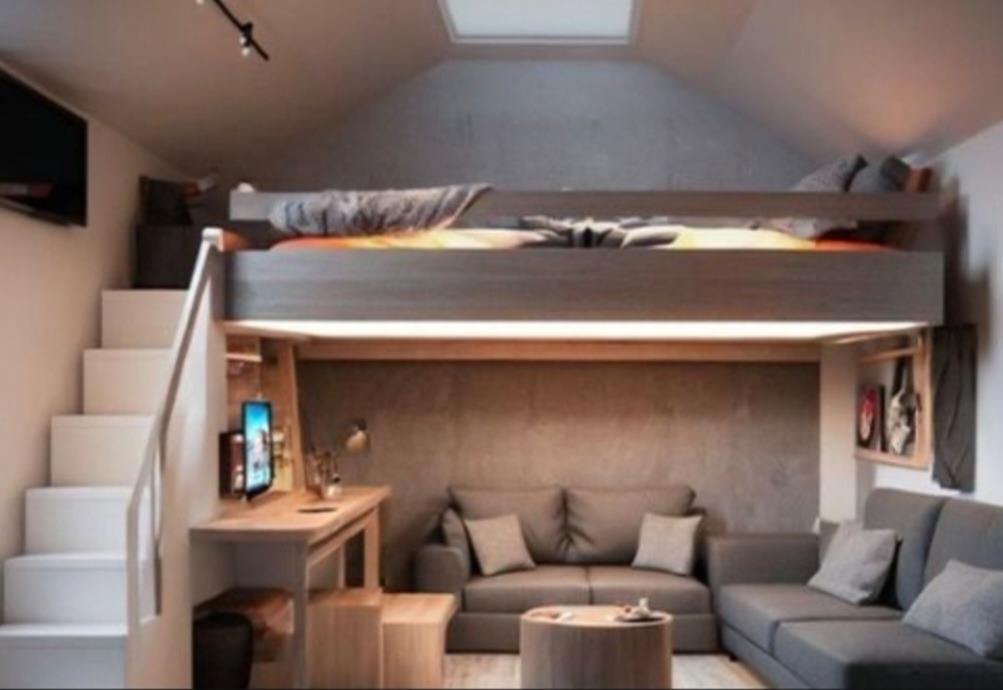 Wielofunkcyjna przestrzeń w pokoju na poddaszu: łóżko na antresoli nad strefą wypoczynkową z szarą sofą narożną i biurkiem, oświetlenie punktowe i okno dachowe.