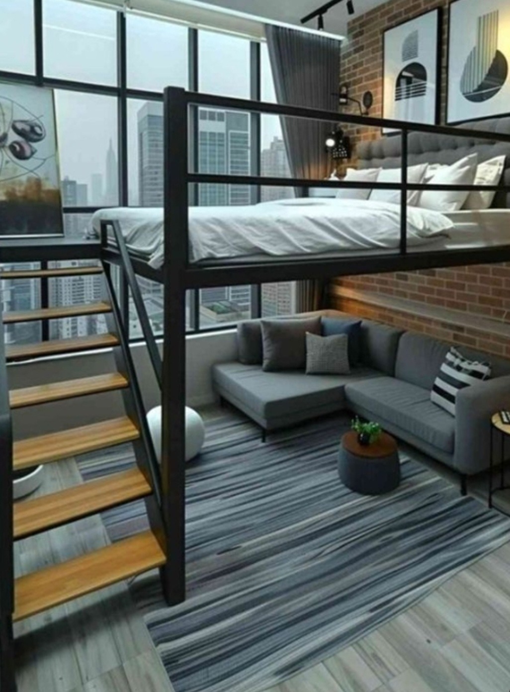 Loftowe mieszkanie z antresolą sypialną, szara sofa narożna, dywan w paski i widok na miasto przez duże okna.