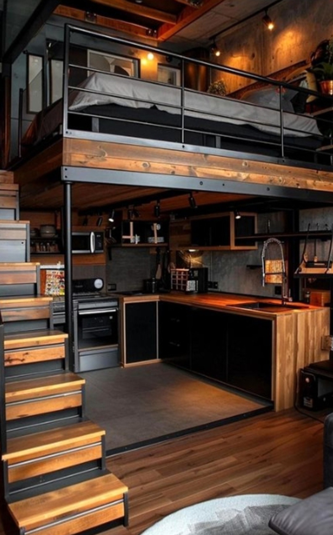 Loftowe mieszkanie w Kątach Wrocławskich z antresolą sypialnianą nad kuchnią. Widoczne drewniane schody, czarne szafki kuchenne z drewnianym blatem i stalowa konstrukcja antresoli.