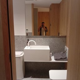 KOLIN BUD - Nowoczesna łazienka z umywalką nablatową, szarą płytką i drewnianymi panelami, widoczne odbicie fotografa w lustrze.