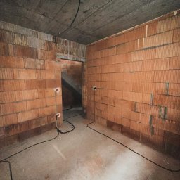 ELEKTRIKVATER SPÓŁKA Z OGRANICZONĄ ODPOWIEDZIALNOŚCIĄ - Surowy stan wnętrza w Warszawie: ściany z czerwonej cegły, betonowy sufit, wystające kable elektryczne z puszkami instalacyjnymi, widok na schody w głębi.