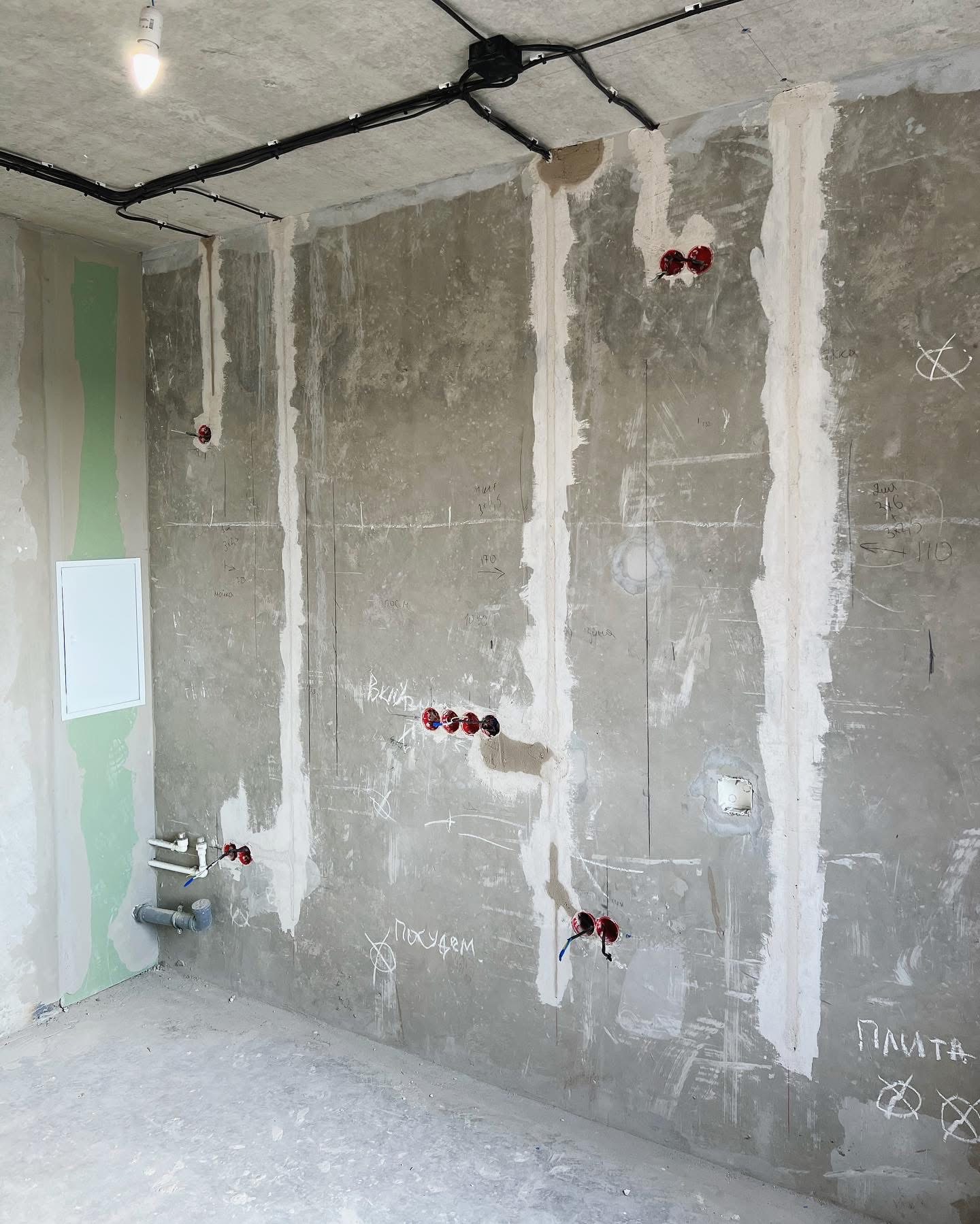 Surowy stan wnętrza w trakcie prac instalacyjnych: widoczne kable elektryczne prowadzone po suficie, puszki instalacyjne w ścianach oraz rury kanalizacyjne przy podłodze, ściany w stanie...