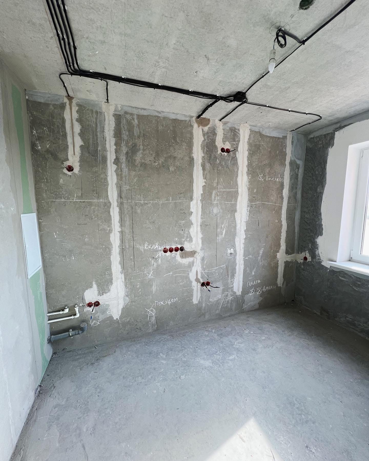 Surowa ściana w trakcie remontu z widocznymi przewodami elektrycznymi, instalacją hydrauliczną i surowym oświetleniem, przygotowana do dalszych prac wykończeniowych.