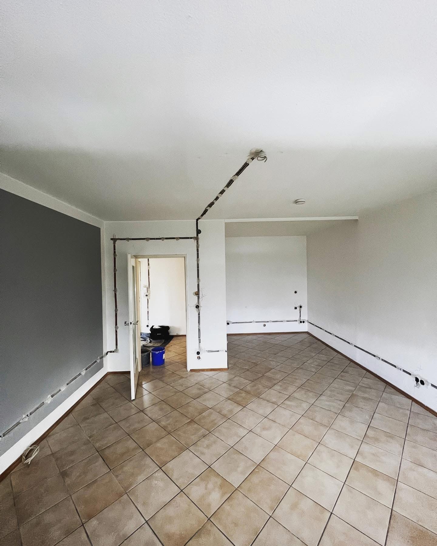 Wnętrze pokoju w trakcie remontu elektrycznego, z widocznymi przewodami elektrycznymi prowadzonymi po ścianach i suficie, przygotowane do montażu gniazdek i oświetlenia.