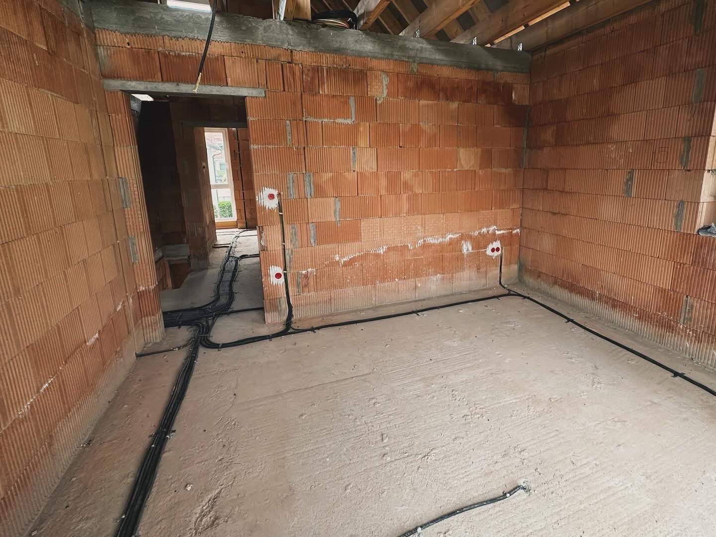 Surowy stan wnętrza z cegły ceramicznej z widocznymi, poprowadzonymi przewodami elektrycznymi wzdłuż ścian i podłogi, przygotowane punkty pod gniazdka.