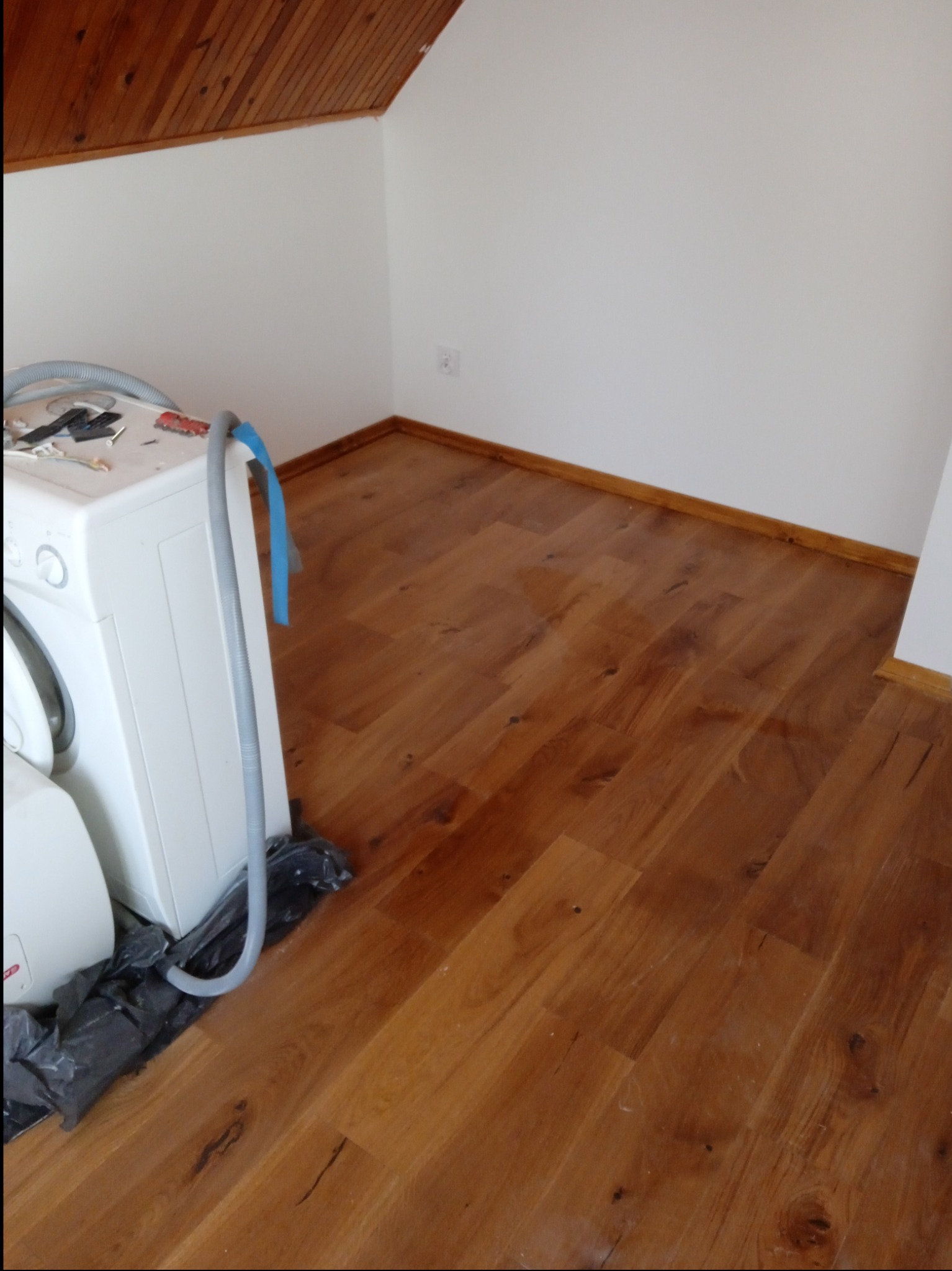 Ukończona podłoga z paneli drewnopodobnych w łazience na poddaszu, pralka częściowo widoczna, narzędzia na pralce, listwy przypodłogowe zamontowane.