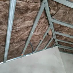 Ocieplenie poddasza wełną mineralną z widoczną konstrukcją metalową i fragmentem ściany z płyt gipsowo-kartonowych przed szpachlowaniem.