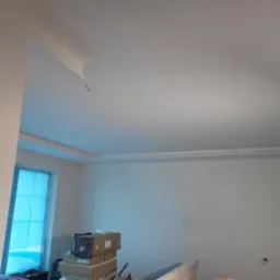 Białe, świeżo pomalowane ściany i sufit w jasnym pomieszczeniu z oknem zabezpieczonym folią, z widocznymi narzędziami i materiałami malarskimi.