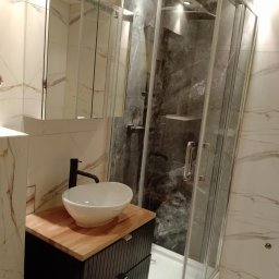 MAX-BUD JAKUB ZARZYŃSKI - Nowoczesna łazienka z kabiną prysznicową typu walk-in, umywalką nablatową na drewnianym blacie i lustrzaną szafką. Marmurowe płytki na ścianach i podłodze.
