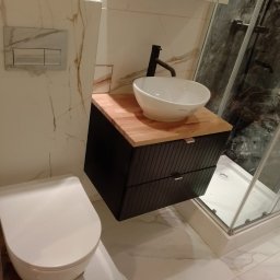 MAX-BUD JAKUB ZARZYŃSKI - Nowoczesna łazienka z umywalką nablatową, czarną szafką z drewnianym blatem i kabiną prysznicową. Marmurowe płytki na ścianach i podłodze.