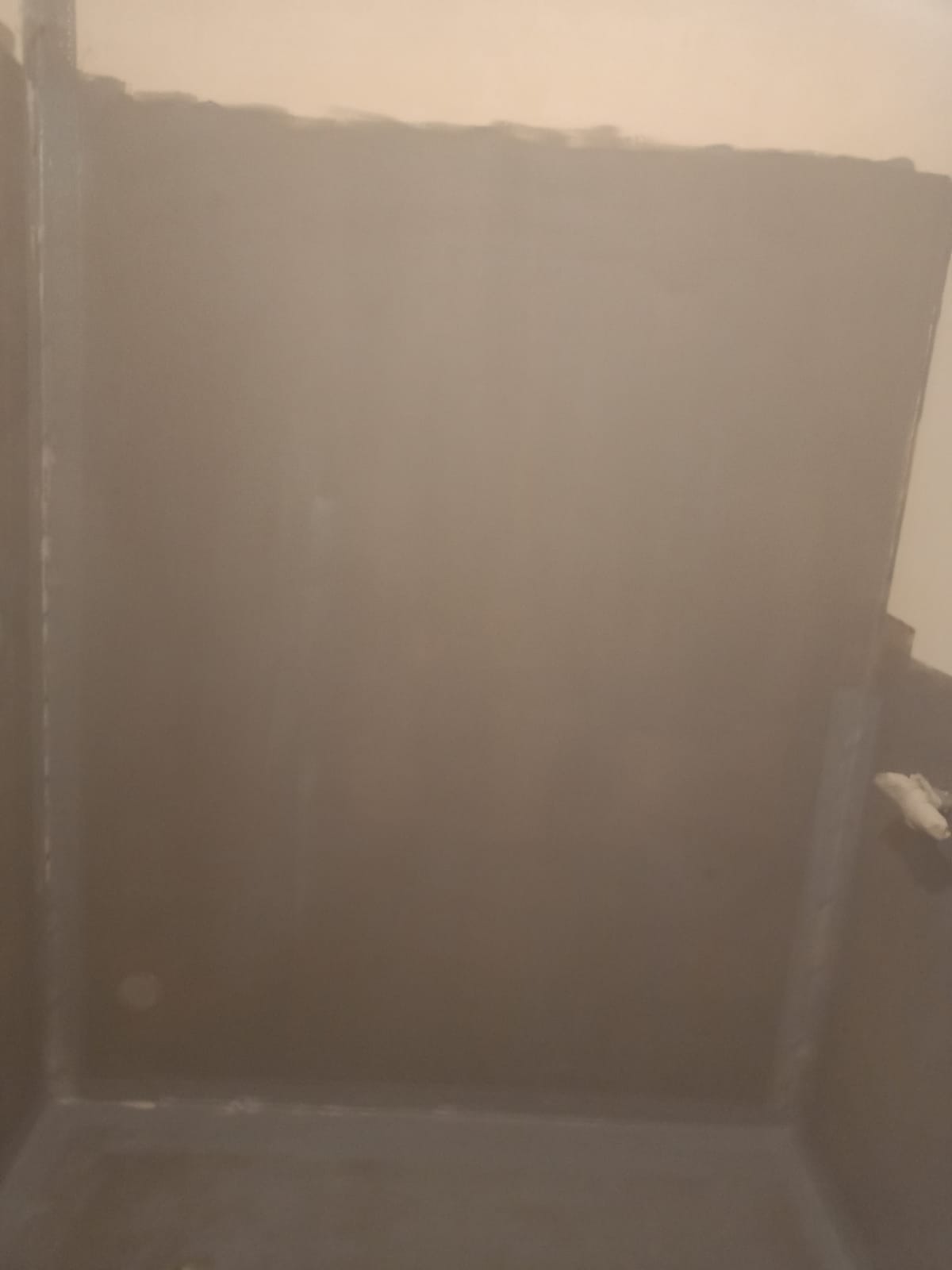 Szara, świeżo nałożona hydroizolacja w rogu łazienki, widoczne niedociągnięcia na górnej krawędzi. Przygotowanie do dalszych prac wykończeniowych.