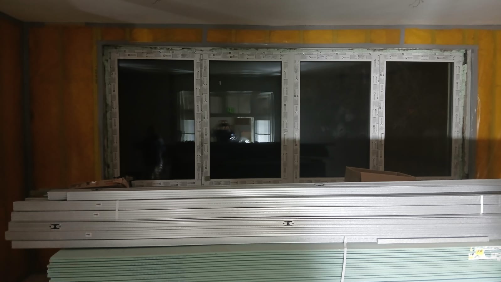 Trzyczęściowe okno PCV w trakcie montażu, widoczne materiały izolacyjne i płyty gipsowo-kartonowe. Etap prac wykończeniowych wewnątrz budynku.