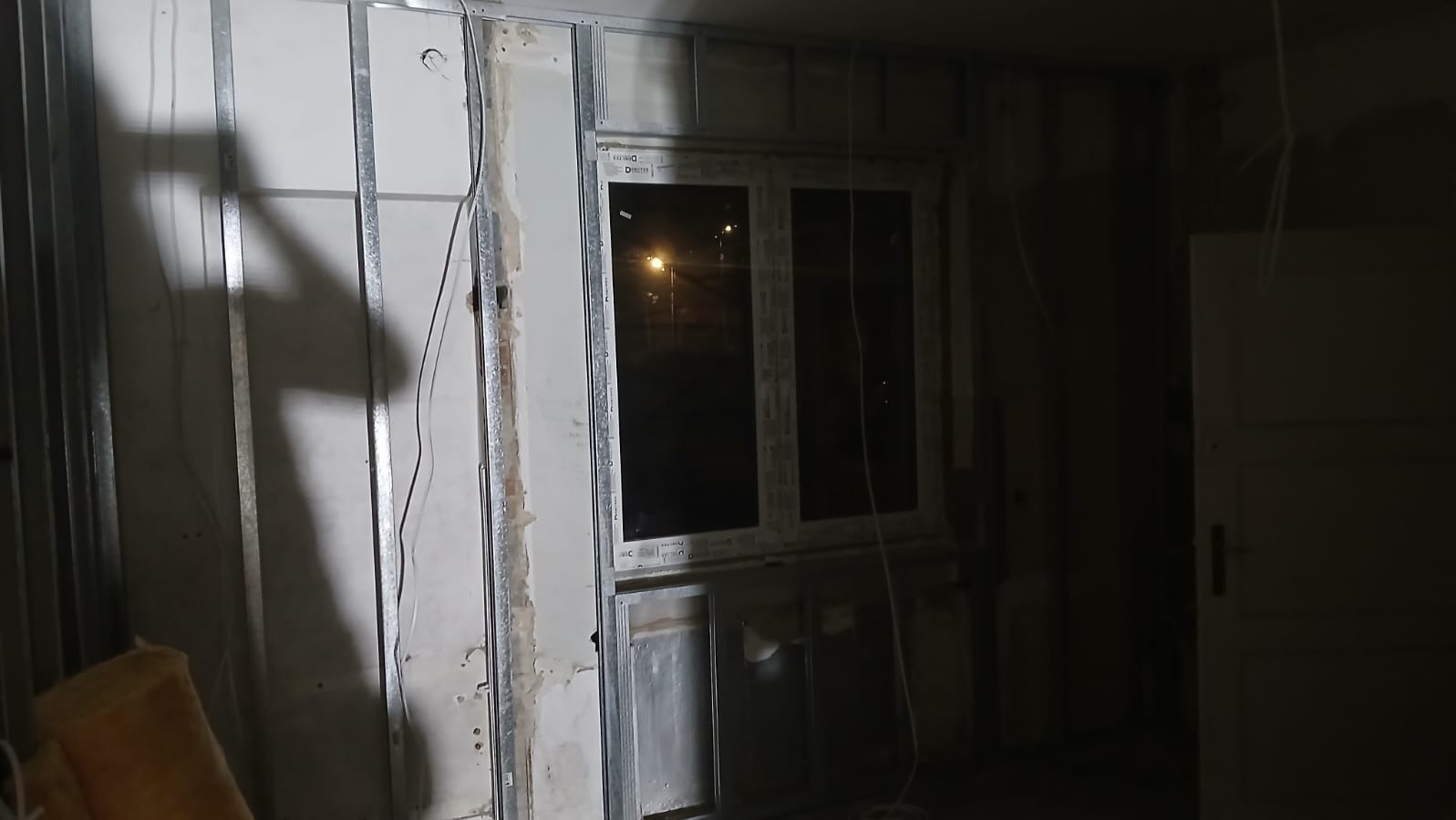 Montaż ścian działowych z płyt gipsowo-kartonowych na metalowym stelażu, widoczne okno i instalacje. Etap prac wykończeniowych w pomieszczeniu.