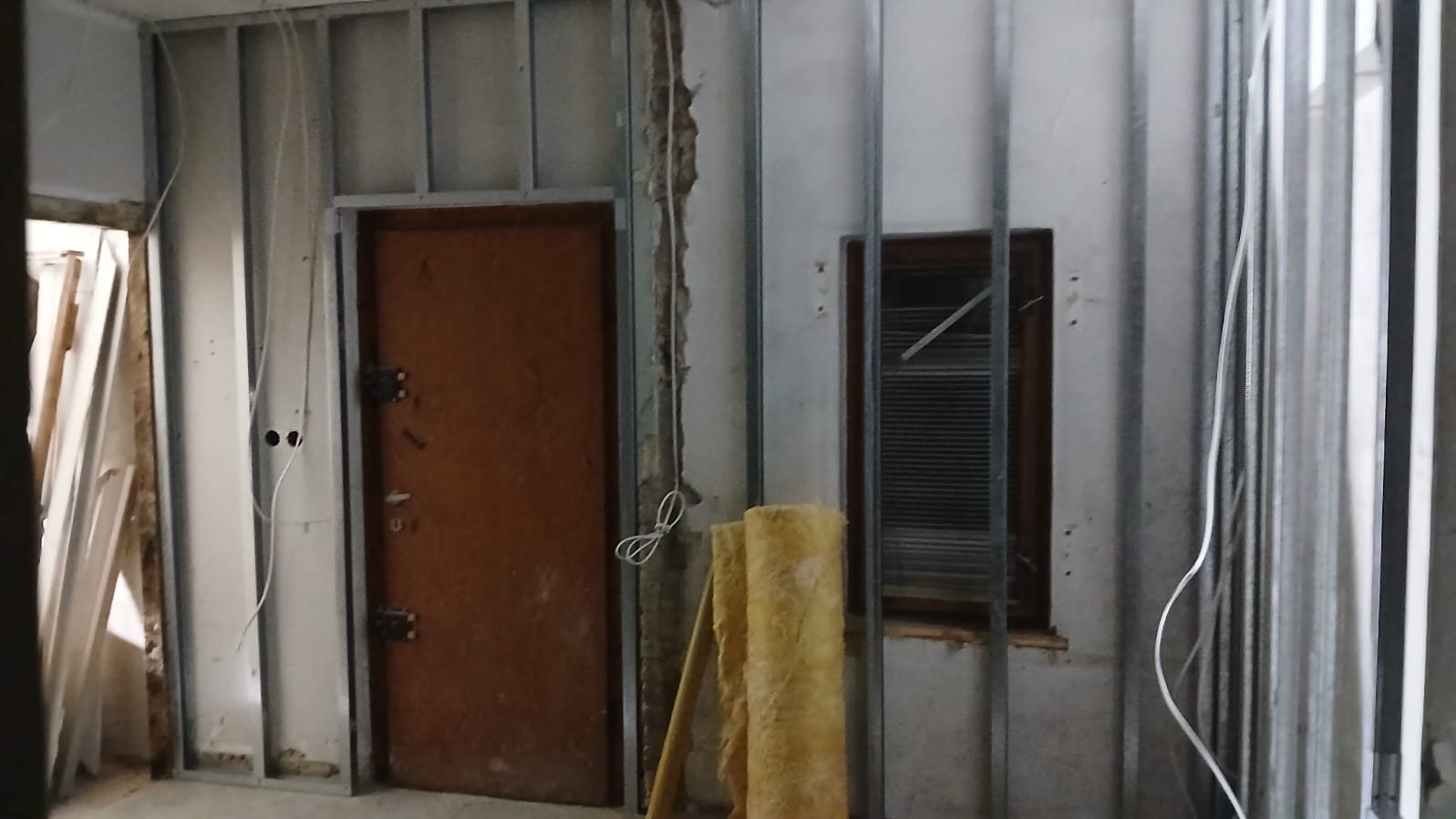 Remont pokoju: metalowy stelaż pod płyty gipsowe, stara stolarka drzwiowa i okienna, ocieplenie w rolce. Etap prac wykończeniowych przed malowaniem ścian.