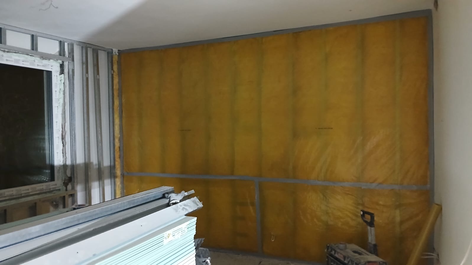 Ocieplenie ściany wełną mineralną w metalowym stelażu, widoczne płyty gipsowe i narzędzia. Etap prac wykończeniowych wewnątrz pomieszczenia.