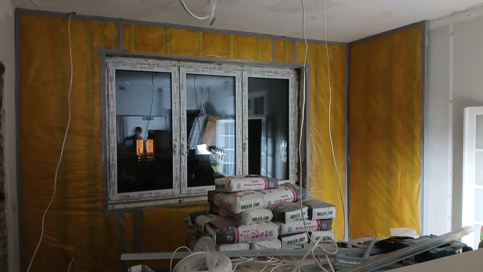 Ocieplanie ścian folią i montaż okna w Gdyni. W tle widoczne worki z klejem gipsowym. Prace wykończeniowe w trakcie realizacji.