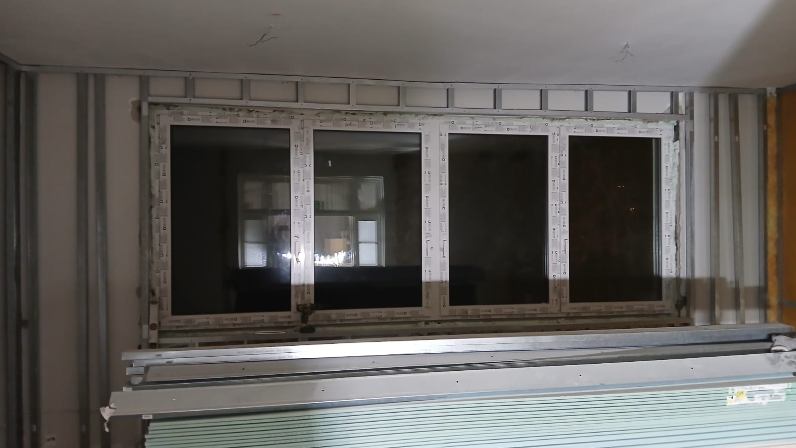 Montaż okna PCV w ścianie z profili metalowych i płyt gipsowo-kartonowych. Widoczne materiały budowlane. Etap prac wykończeniowych.