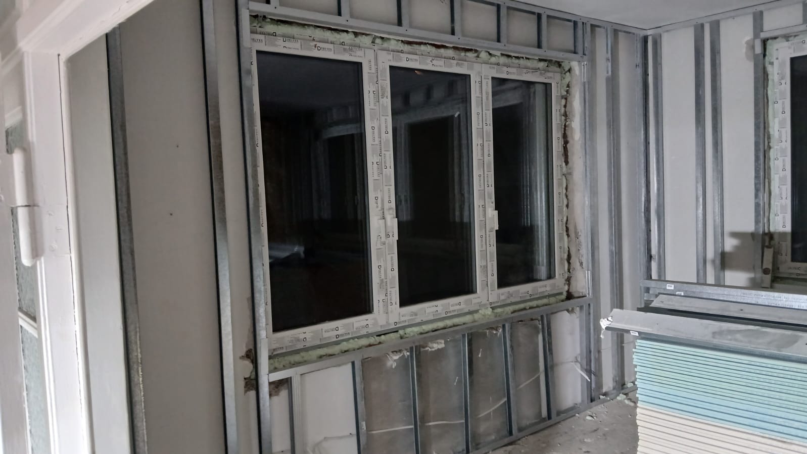 Montaż okien w ramie z profili stalowych, widoczne płyty gipsowo-kartonowe. Etap prac wykończeniowych w pomieszczeniu z oknami PCV.