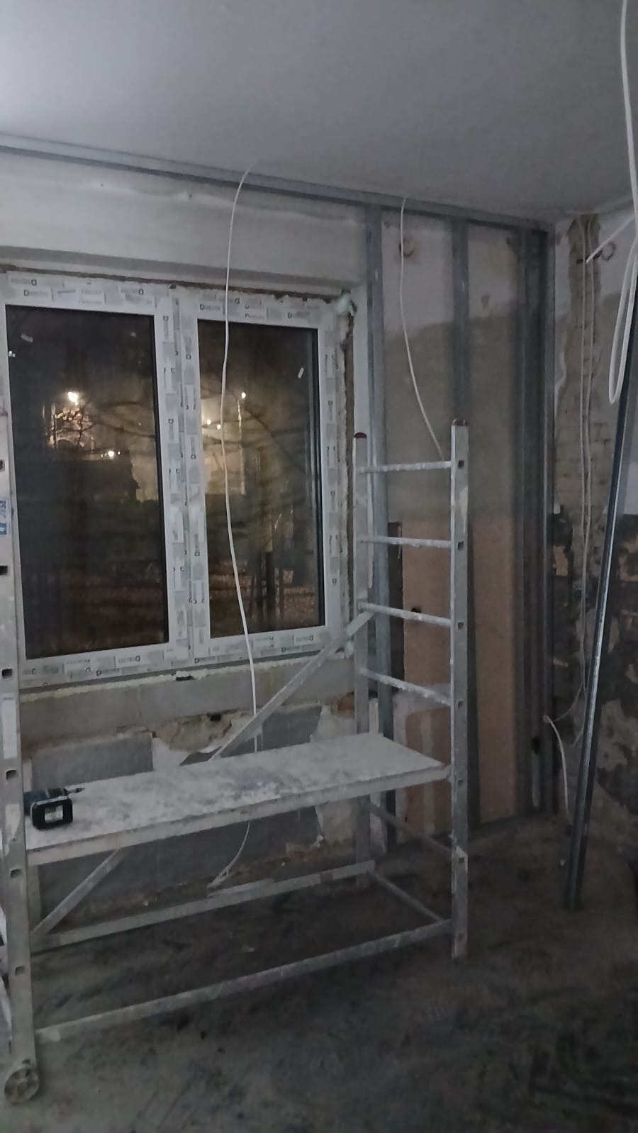 Montaż profili pod płytę gipsową przy oknie, widoczne kable i rusztowanie. Etap prac wykończeniowych w pomieszczeniu z oknem.