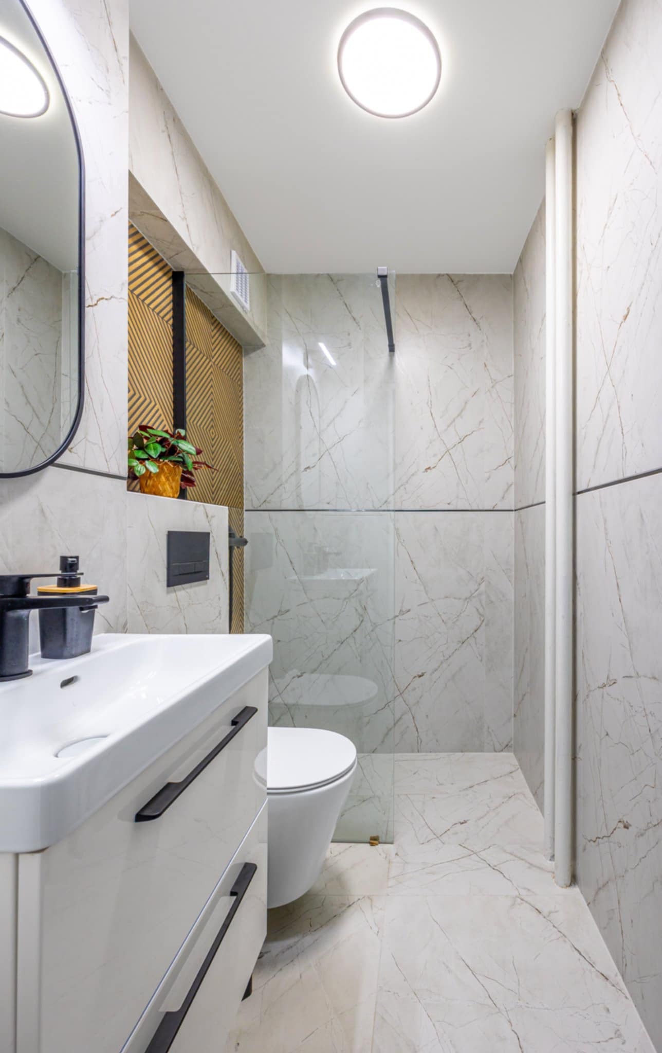 Nowoczesna łazienka z marmurowymi płytkami, czarną armaturą i geometrycznym akcentem na ścianie. Umywalka z szafką, toaleta i kabina prysznicowa.