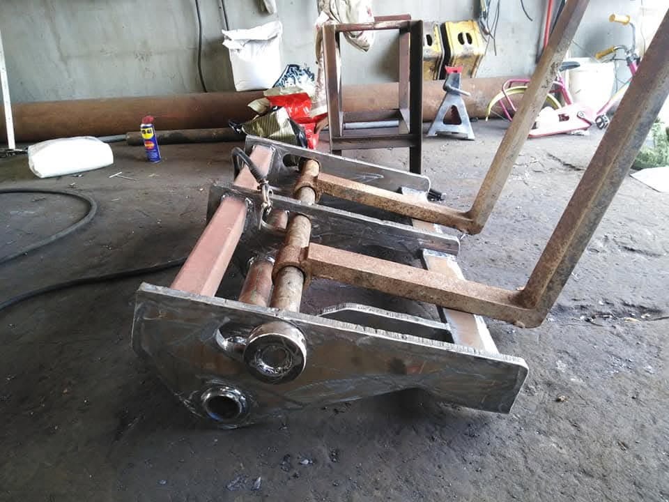 Metalowa konstrukcja wideł do wózka widłowego w trakcie budowy, z widocznymi elementami po obróbce, leżąca na brudnej posadzce warsztatu.