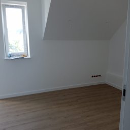 Usługi Remontowe Bez Problemu - Poddasze po remoncie: świeżo pomalowane białe ściany, jasne panele podłogowe, okno z białymi ramami, widoczne gniazdka elektryczne bez osprzętu.