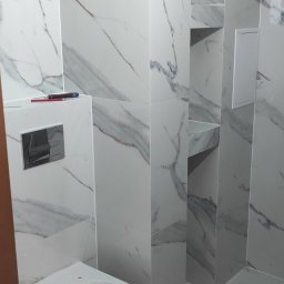 Usługi Remontowe Bez Problemu - Montaż wiszącej toalety na tle marmurowych płytek, widoczne narzędzia glazurnicze na podłodze oraz wnęki w ścianie.