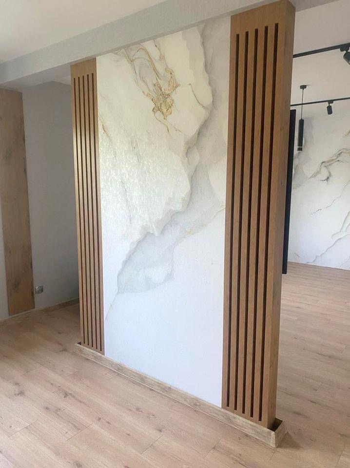Nowoczesna ścianka działowa z marmurowym wzorem i drewnianymi lamelami, oddzielająca przestrzeń w jasnym wnętrzu z panelami podłogowymi.