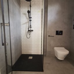 TPBUDOWA - Nowoczesna łazienka z kabiną prysznicową typu walk-in z czarną armaturą i geometryczną mozaiką na ścianie, wisząca toaleta.