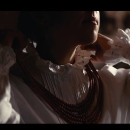 SOULmedia Marcin Dusza - Kobieta w białej bluzce z koronkowym kołnierzem zakłada wielorzędowy korale z ciemnoczerwonych koralików w ciepłym oświetleniu.