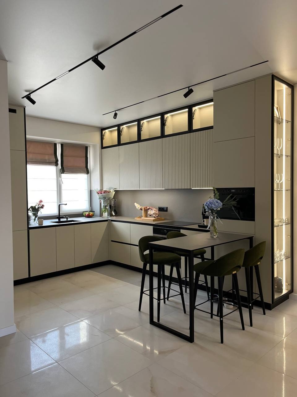 Nowoczesna kuchnia z oświetleniem szynowym i barkiem w Bytowie. Kremowe szafki z czarnymi akcentami, marmurowa podłoga, eleganckie wykończenie wnętrza.