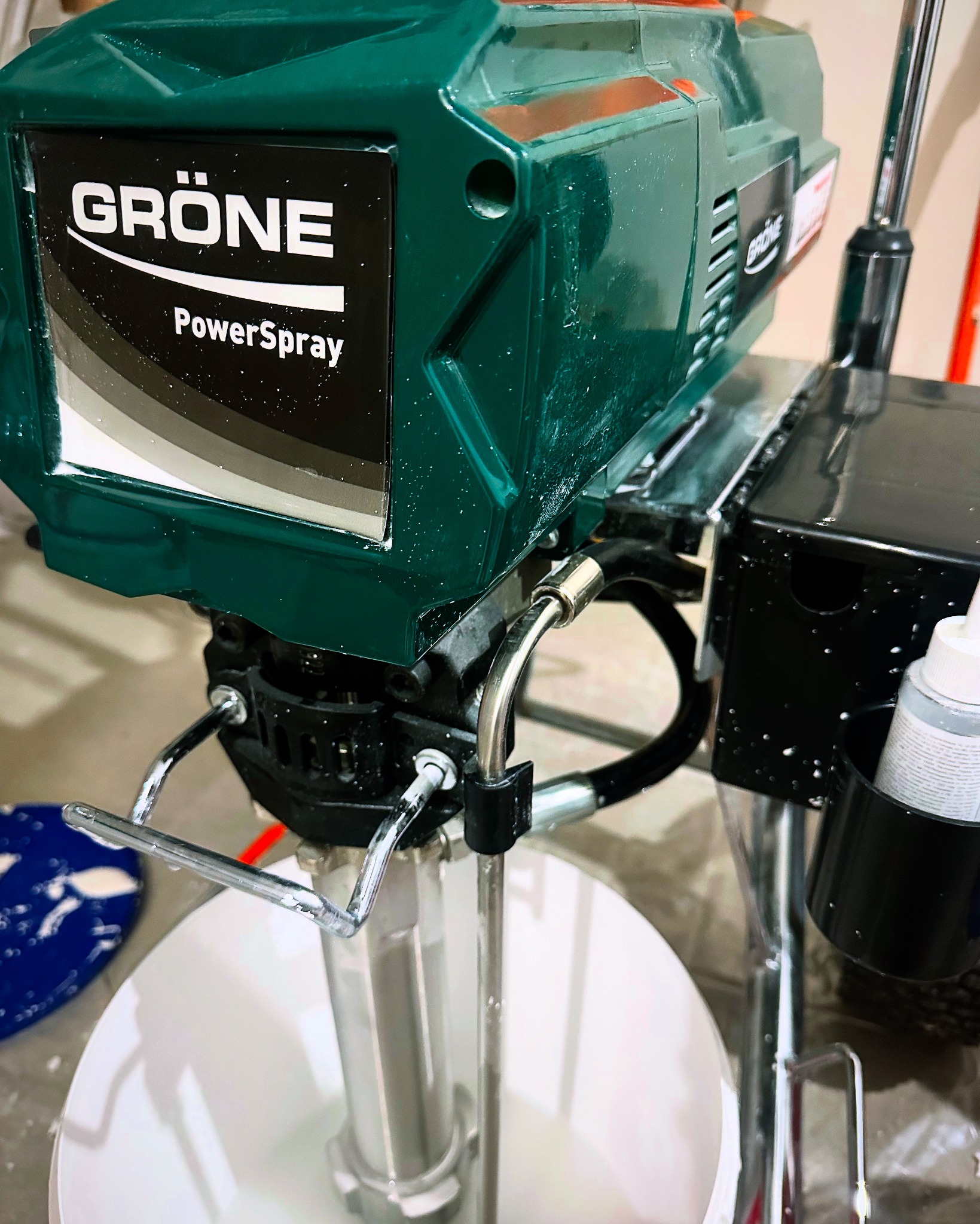 Zielony agregat malarski Gröne PowerSpray z widocznymi śladami farby, stojący na wiadrze z farbą.