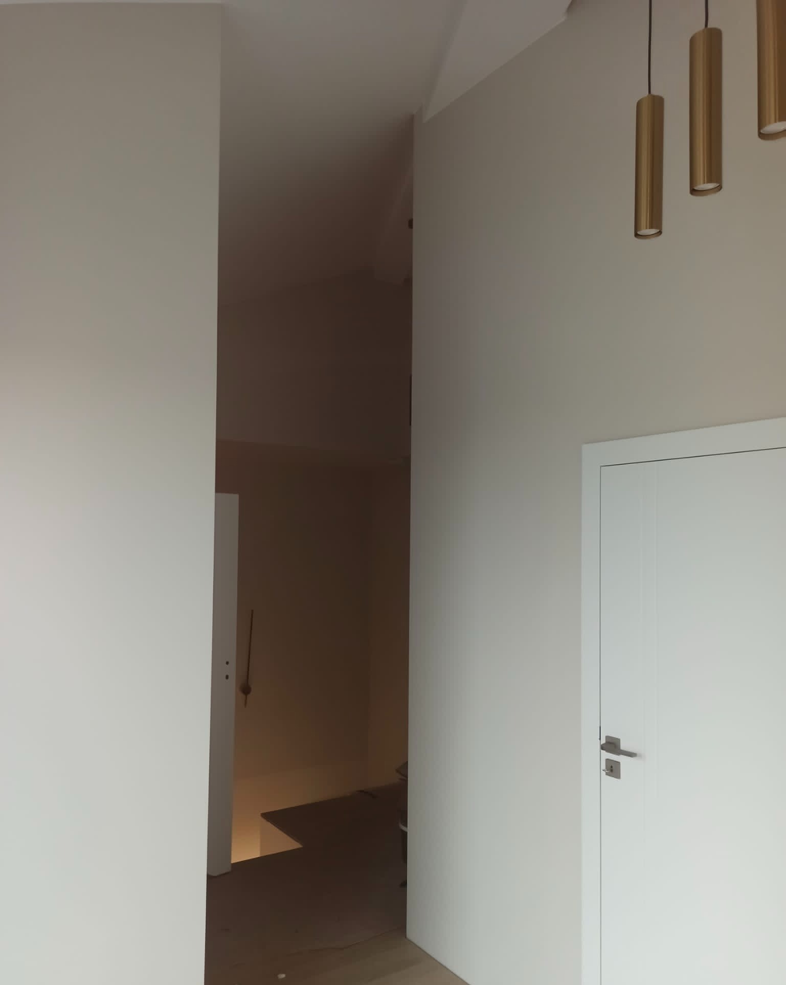Jasne, świeżo pomalowane wnętrze z białymi drzwiami i złotymi lampami wiszącymi, widok na korytarz z przygotowanym podłożem.