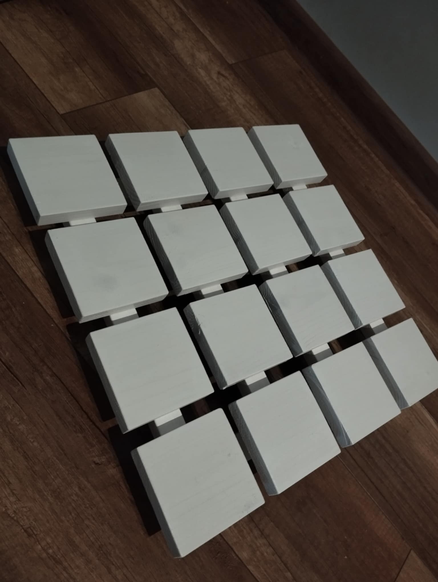 Kwadratowe panele z białego drewna ułożone na podłodze z paneli, tworzące dekoracyjny wzór.