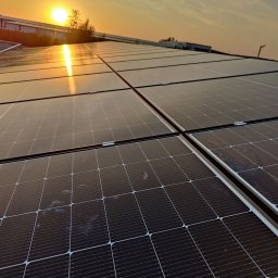 EKOZYSK Grzegorz Kotecki - Instalacja fotowoltaiczna na dachu budynku komercyjnego, widok pod kątem, zachodzące słońce odbija się w panelach, widoczne zabrudzenia na powierzchni paneli.