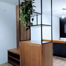 Drewniana szafa z otwartymi półkami i metalową konstrukcją, na jednej z półek doniczka z rośliną, widoczny fragment salonu z szarą sofą.