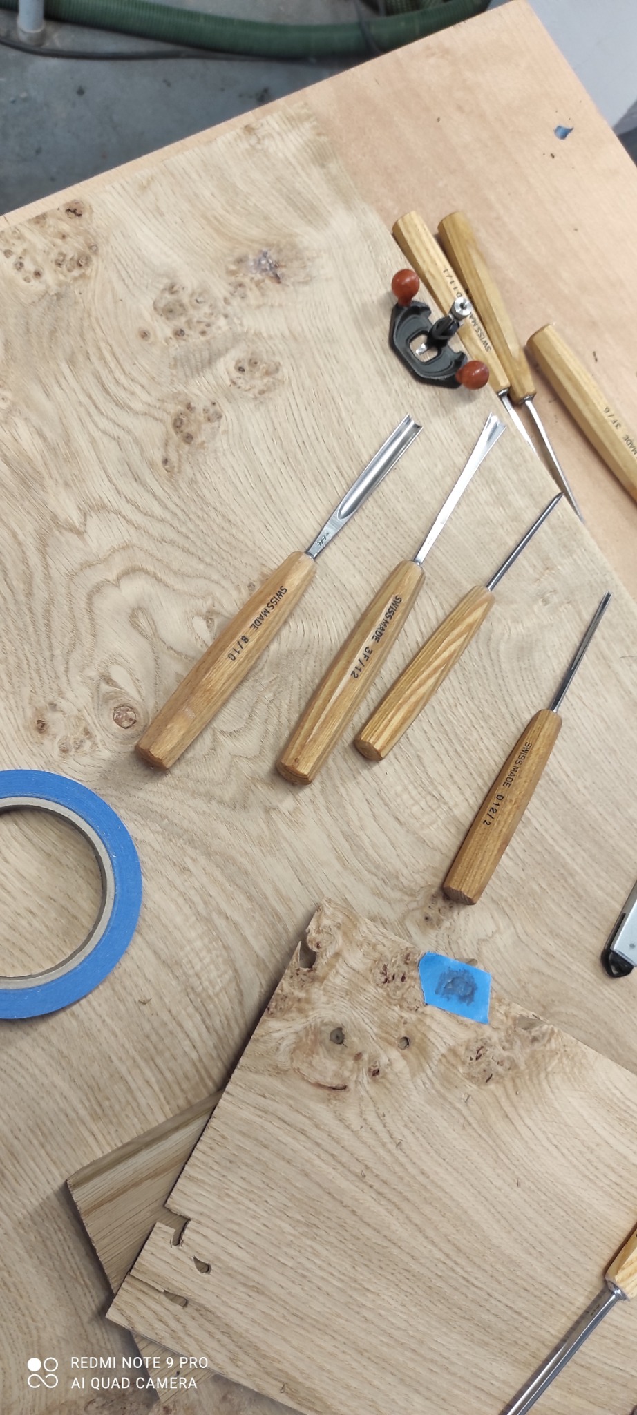 Drewniany blat roboczy z dłutami stolarskimi Swiss Made, niebieską taśmą malarską i fragmentami połączonych desek z widocznym połączeniem na wpust i czop.