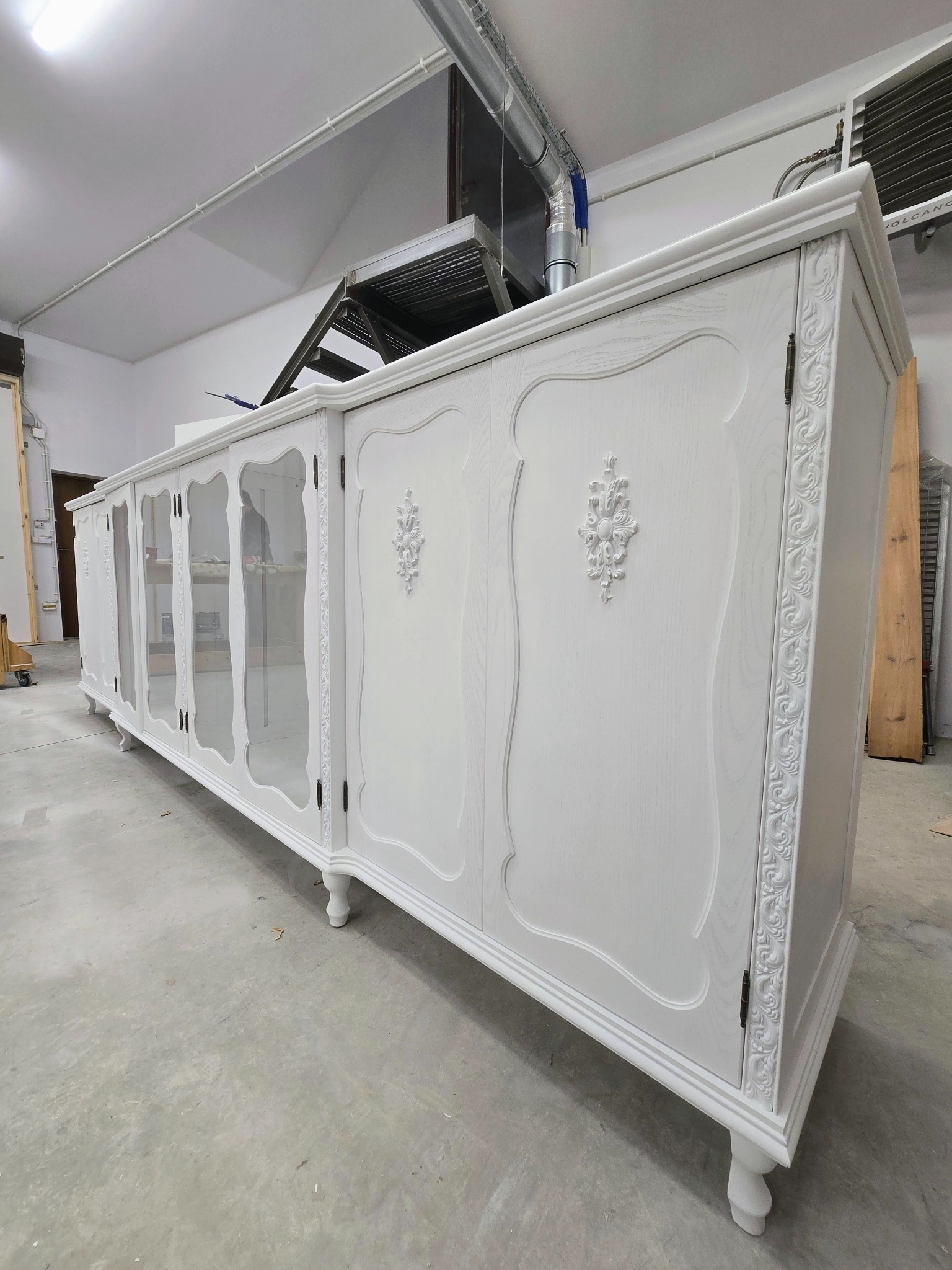 Długa, biała szafa na wymiar z przeszklonymi drzwiami i zdobieniami w stylu retro, wykonana w Borkach Wielkich. Widok z perspektywy podłogi.