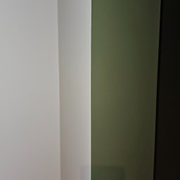 WILEN - Fragment narożnika pokoju z pomalowanymi ścianami: białą i oliwkową, w tle ciemny cień.