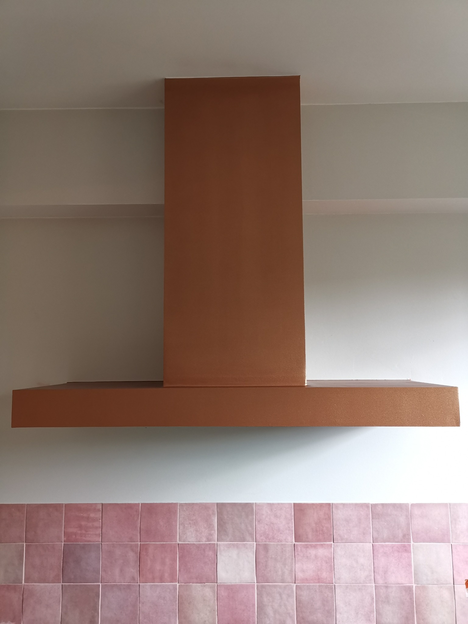 Miedziany okap kuchenny w minimalistycznym stylu, zamontowany nad różowymi płytkami w kuchni w Warszawie.