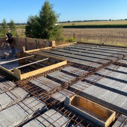 RD-West Bud - Budowa stropu Teriva: betonowe pustaki, stalowe zbrojenie i drewniane szalunki na tle krajobrazu. Widoczny etap prac z osobą w tle.