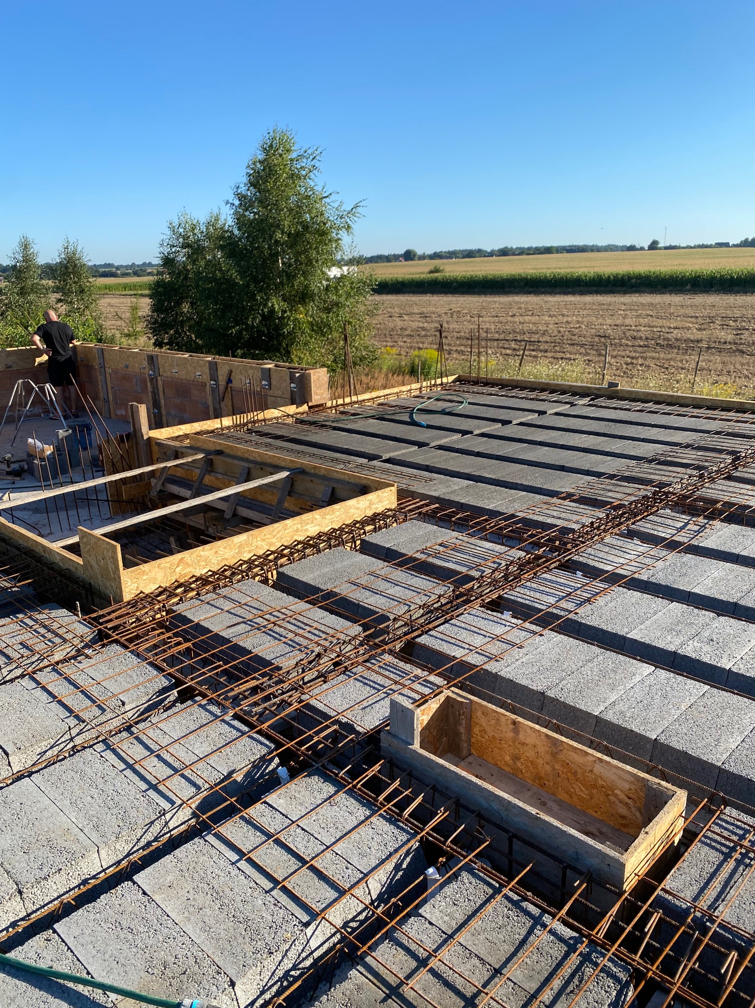 Budowa stropu Teriva: betonowe pustaki, stalowe zbrojenie i drewniane szalunki na tle krajobrazu. Widoczny etap prac z osobą w tle.