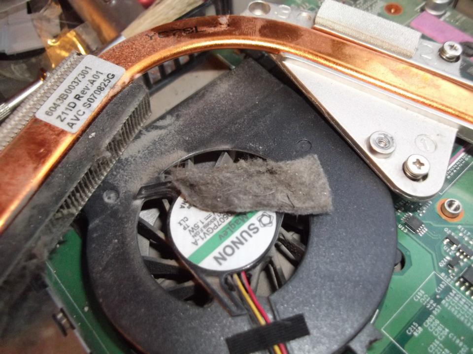 Zabrudzony wentylator notebooka z fragmentem kurzu na łopatkach, widoczny radiator z miedzianą rurką cieplną i fragment płyty głównej.