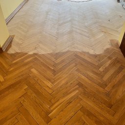 Podlogi Premium Skandynawia - Cyklinowanie parkietu w jodełkę: widoczna różnica między obszarem po cyklinowaniu a obszarem przed obróbką, z maszyną cykliniarską w tle.