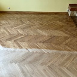 Podlogi Premium Skandynawia - Parkiet ułożony w jodełkę, w połowie wycyklinowany, ukazujący różnicę w kolorze i fakturze przed i po zabiegu, ściana w tle w kolorze żółtym.