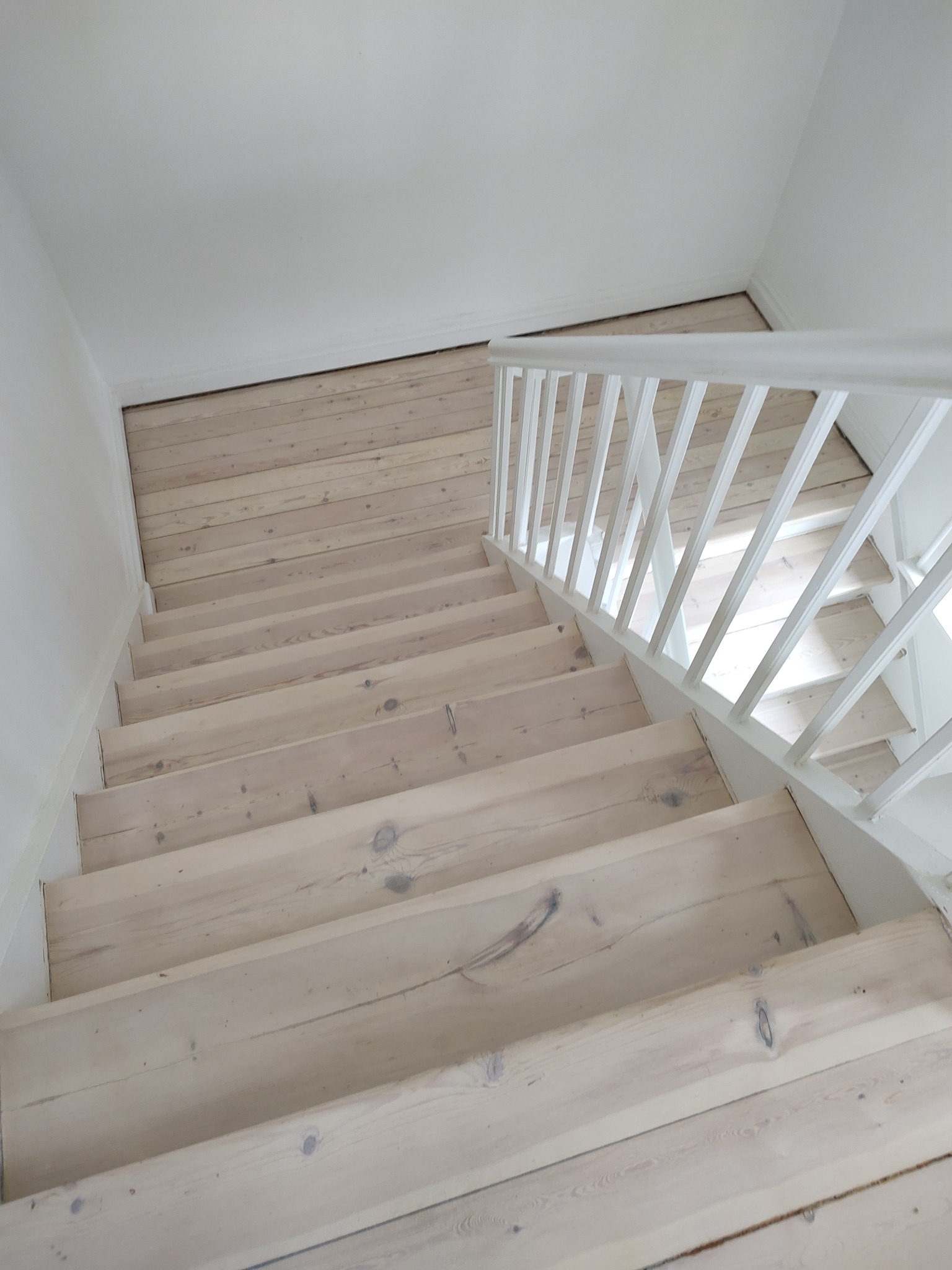Białe drewniane schody po cyklinowaniu, widok z góry, jasne oświetlenie, widoczne słoje drewna i biała balustrada.