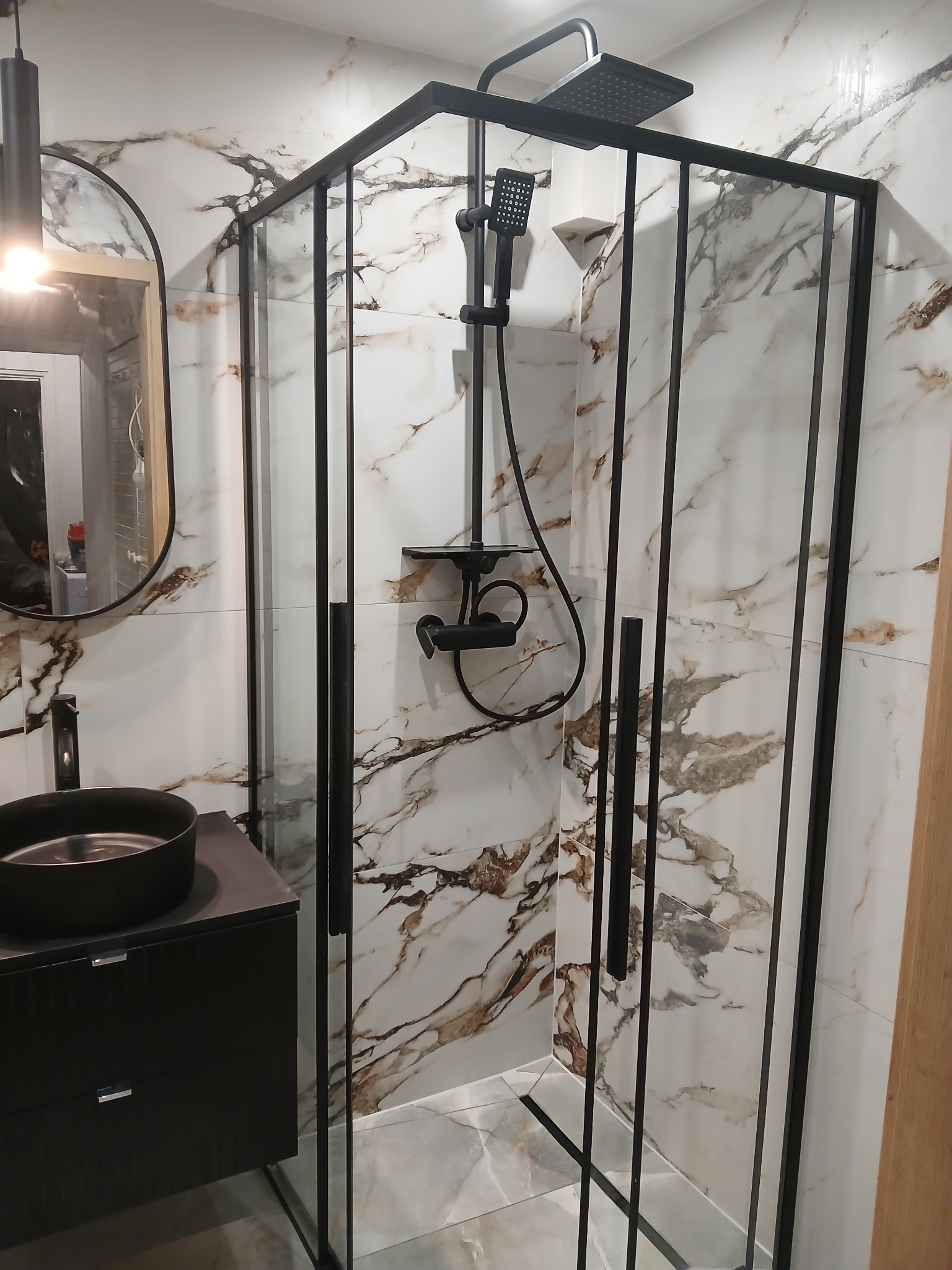 Nowoczesna łazienka z kabiną prysznicową typu walk-in z czarnymi profilami, umywalką nablatową i marmurowymi płytkami ściennymi z brązowymi żyłami.