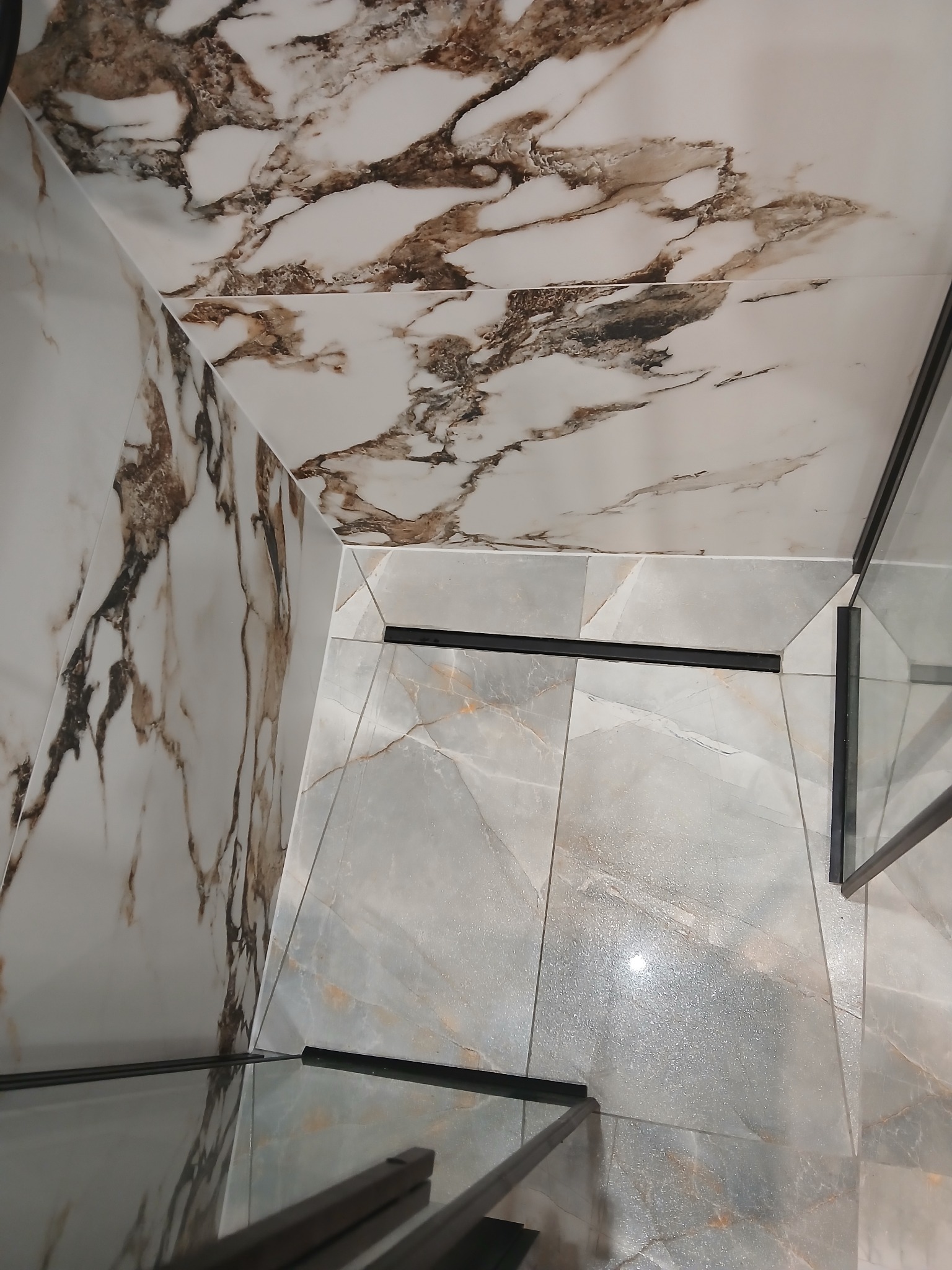 Wykończona kabina prysznicowa z marmurowymi płytkami na ścianach i podłodze, czarne profile kabiny, widok z góry, nowoczesny design.